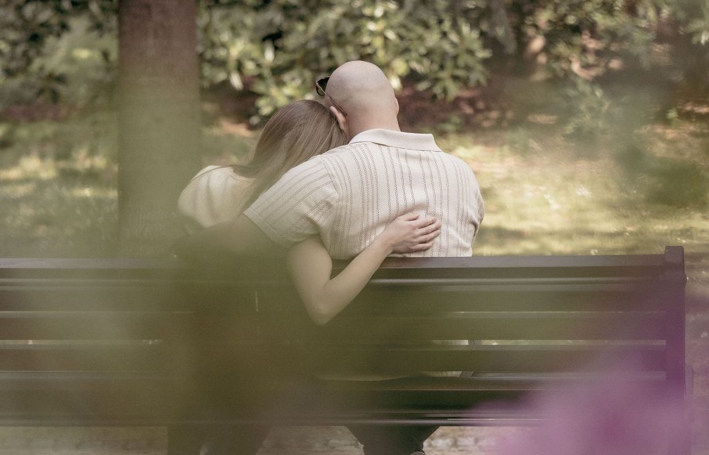 A couple sits on a bench, cuddling, in Villa dei Cedri Park in Bellinzona