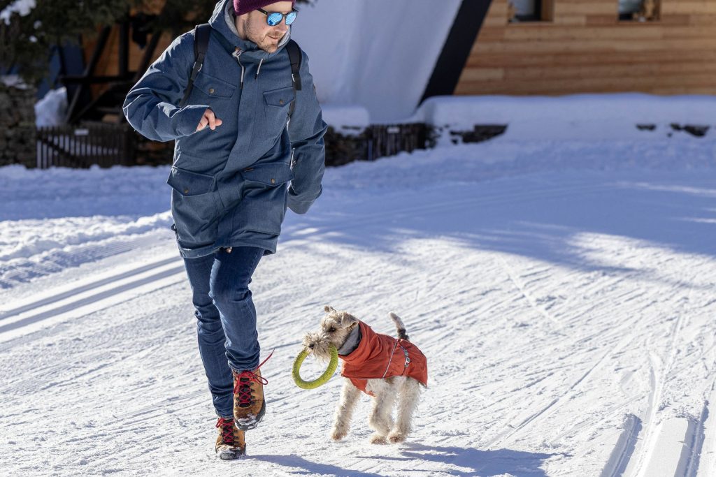 A man is playing with his dog in the snowy mountains in winter in Switzerland