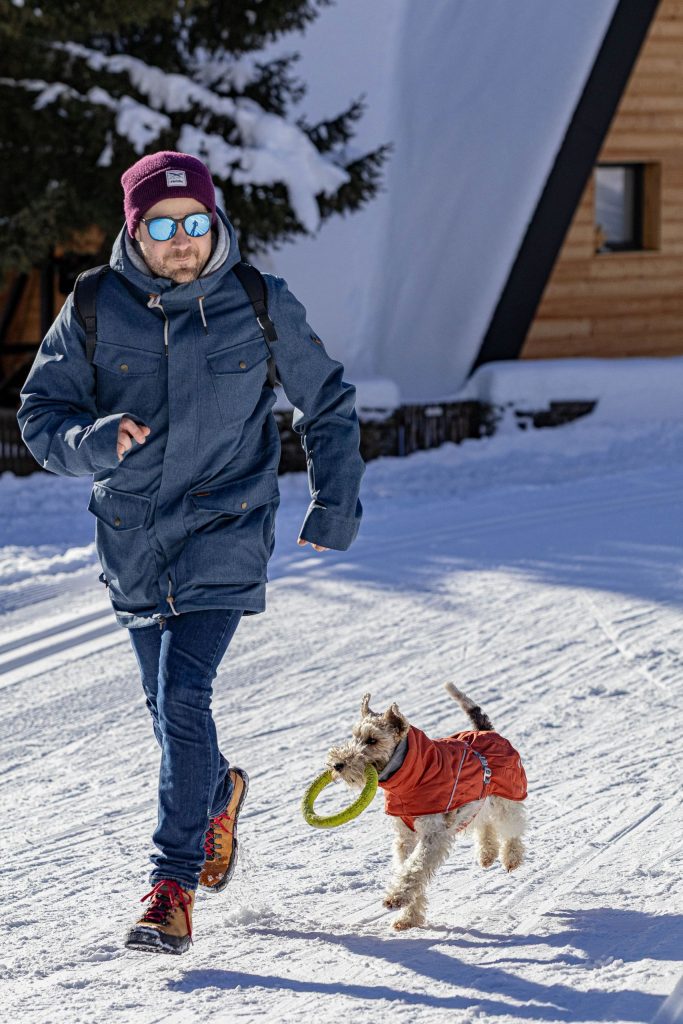 A man is playing with his dog in the snowy mountains in winter in Switzerland