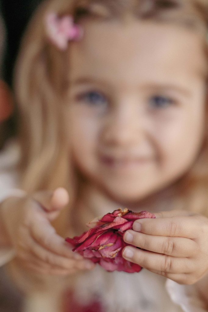 A little girl holds out a red flower toward the camera in Villa dei Cedri Park in Bellinzona