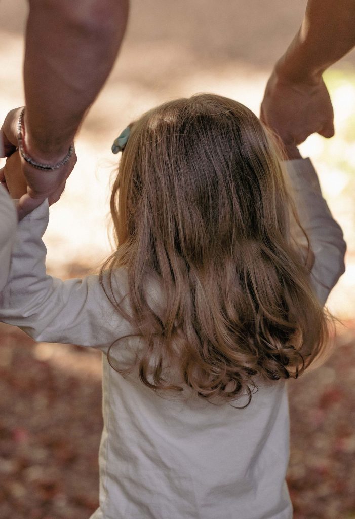 A mother and a father are holding their little girl's hand while walking in the Villa dei Cedri park in Bellizona