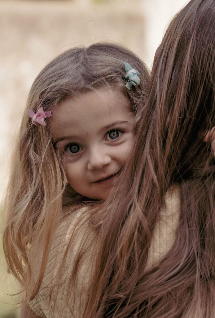 A little girl looks back with a smile over her mother's shoulder in Villa dei Cedri Park in Bellinzona