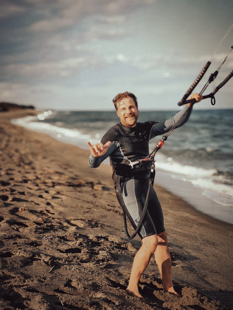 A man sets off to go kitesurfing on the beach, smiling