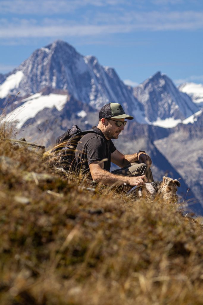 A man is sitting in the grass with his dog in the Swiss Alps in the summer
