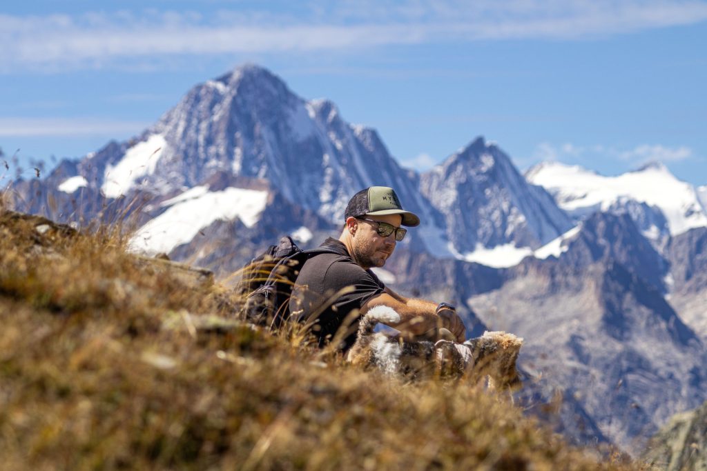A man is sitting in the grass with his dog in the Swiss Alps in the summer