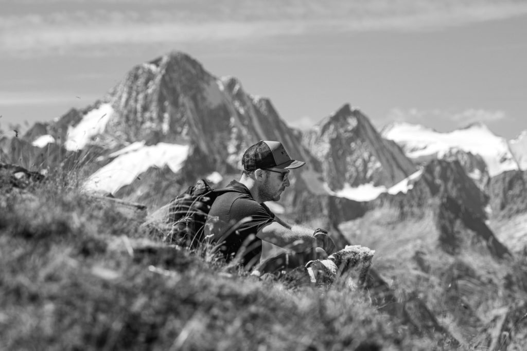 A man is sitting in the grass with his dog in the Swiss Alps in the summer
