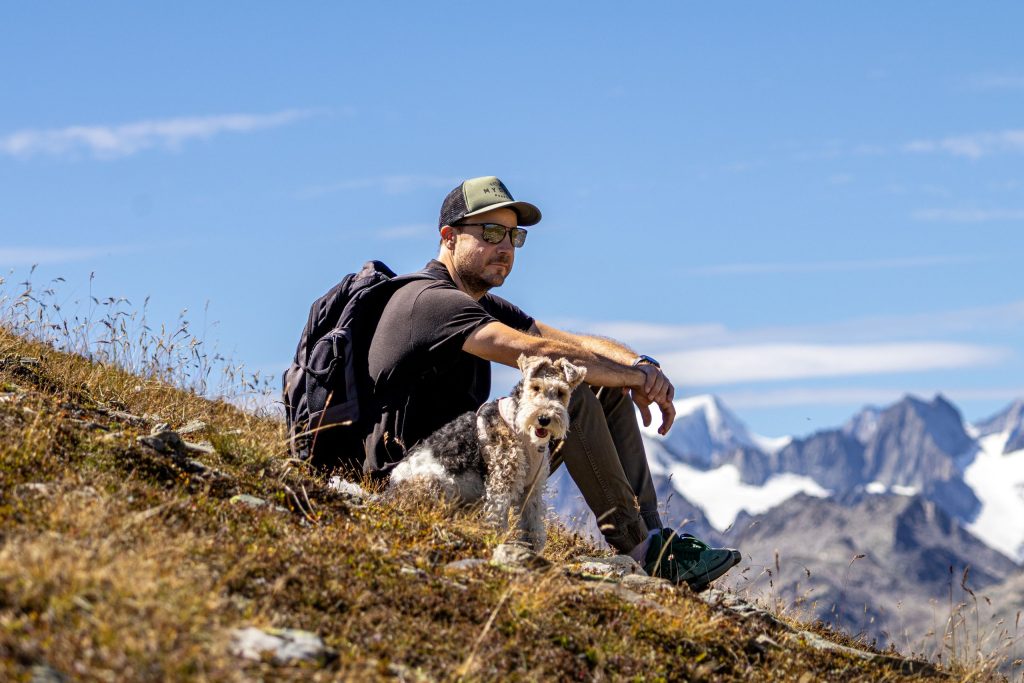 A man is sitting in the grass with his dog in the Swiss Alps in the summer