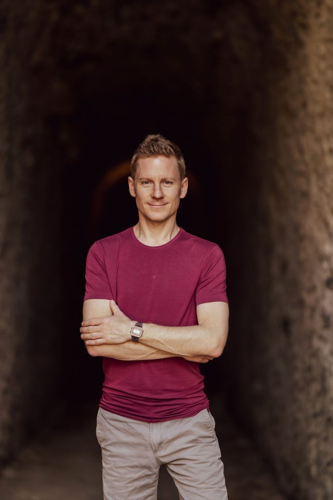 A man smiles at the camera in front of the entrance to a cave at Castel Grande in Bellinzona