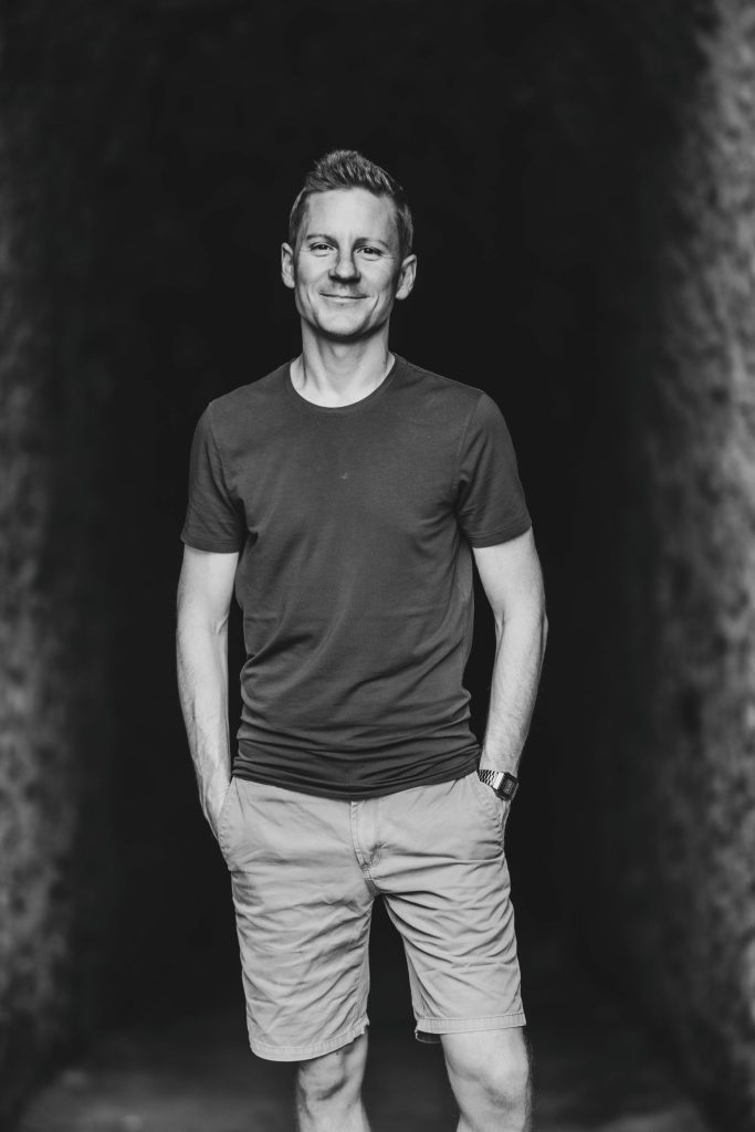A man smiles at the camera in front of the entrance to a cave at Castel Grande in Bellinzona