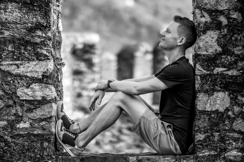 A man is sitting on the castle wall, smiling at Castel Grande in Bellinzona