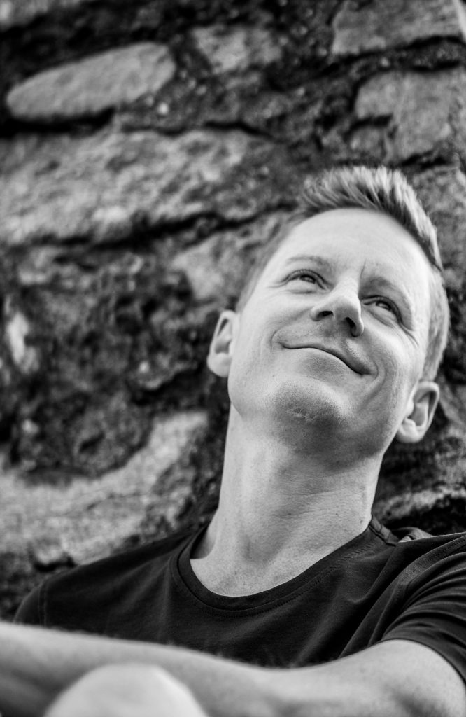 A man is sitting on the castle wall, smiling at Castel Grande in Bellinzona