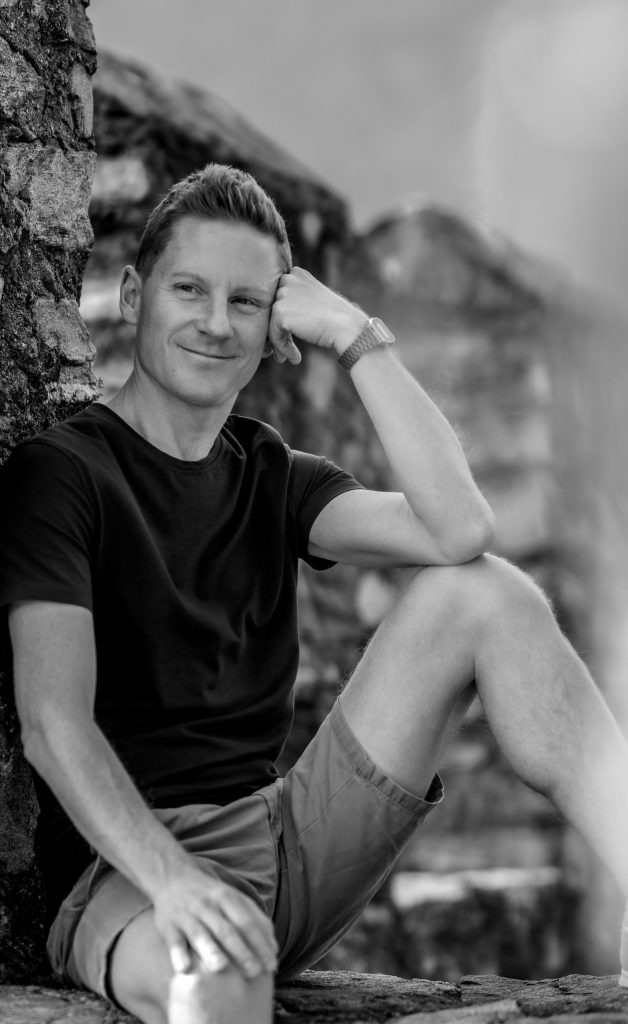 A man is sitting on the castle wall, smiling at Castel Grande in Bellinzona