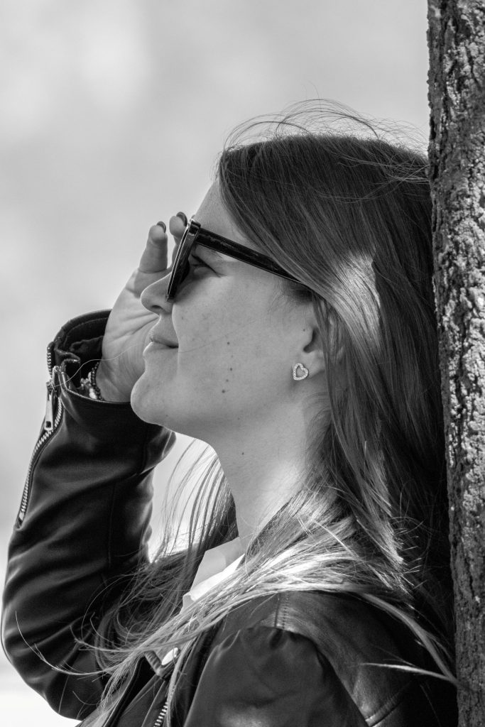 A woman leans against a tree with a smile at Castel Grande in Bellinzona