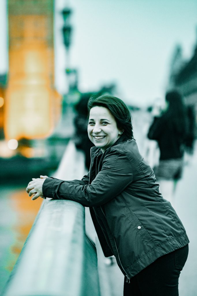 A woman leans against the railing of a bridge in London, in front of Big Ben, laughing