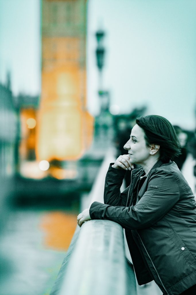 A woman leans against the railing on a bridge in London, in front of Big Ben