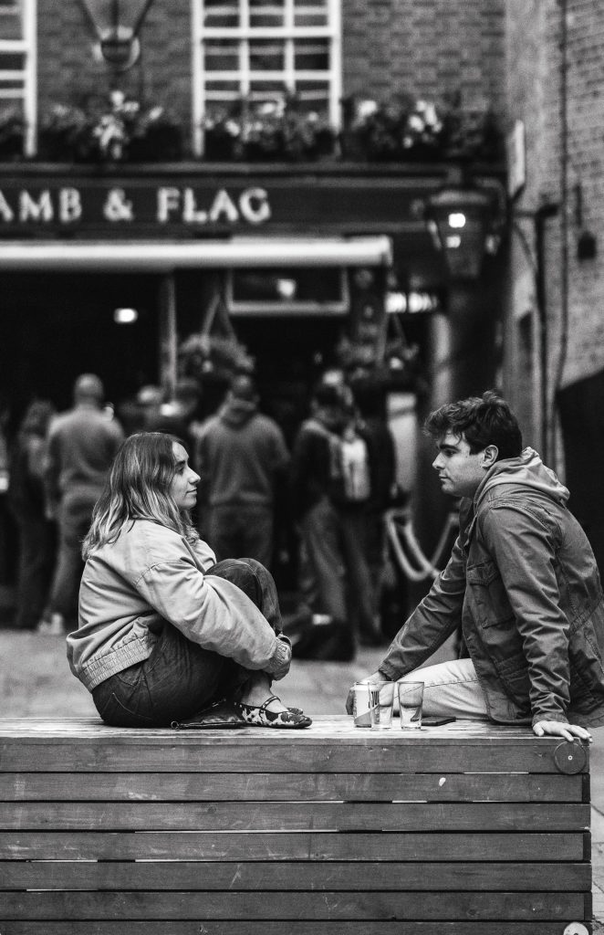 A young couple is talking while sitting across from each other in front of a bar in London